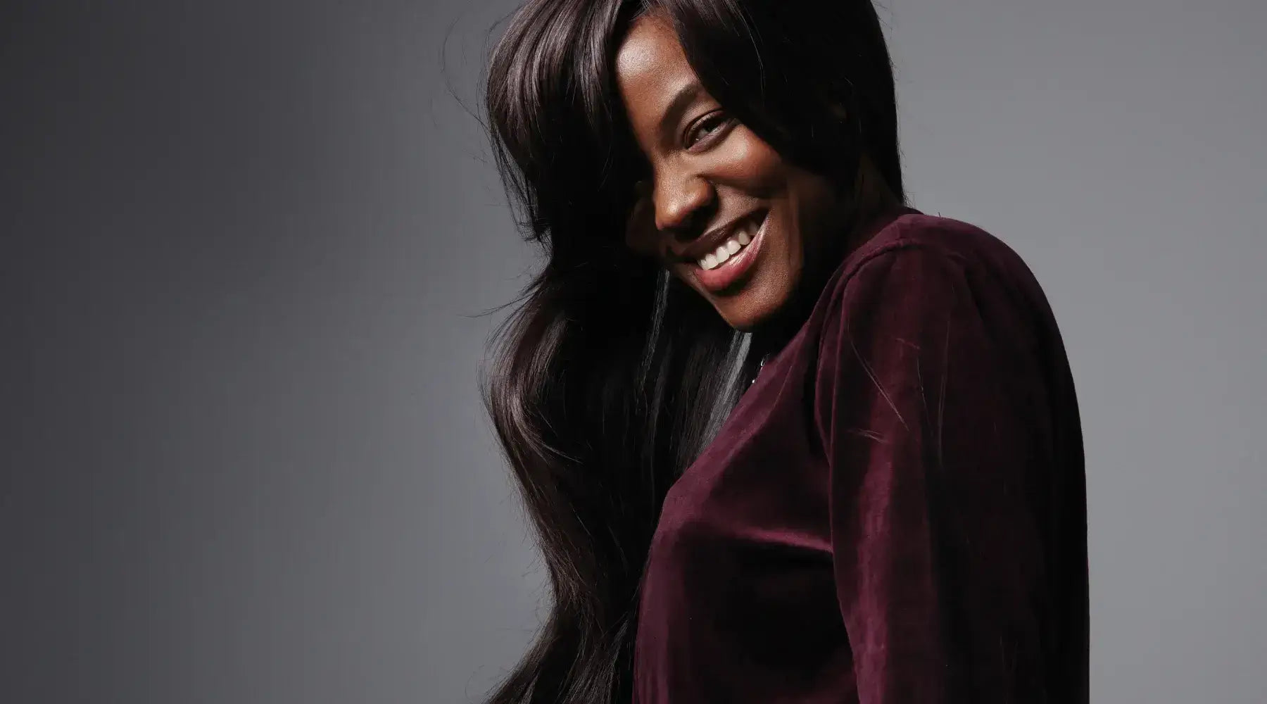 A pretty Black model with a long dark loose wave hairstyle smiling for a portrait