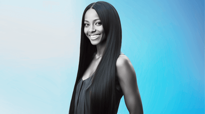 A woman with long silky hair standing partially to the side facing forward smiling for the camera