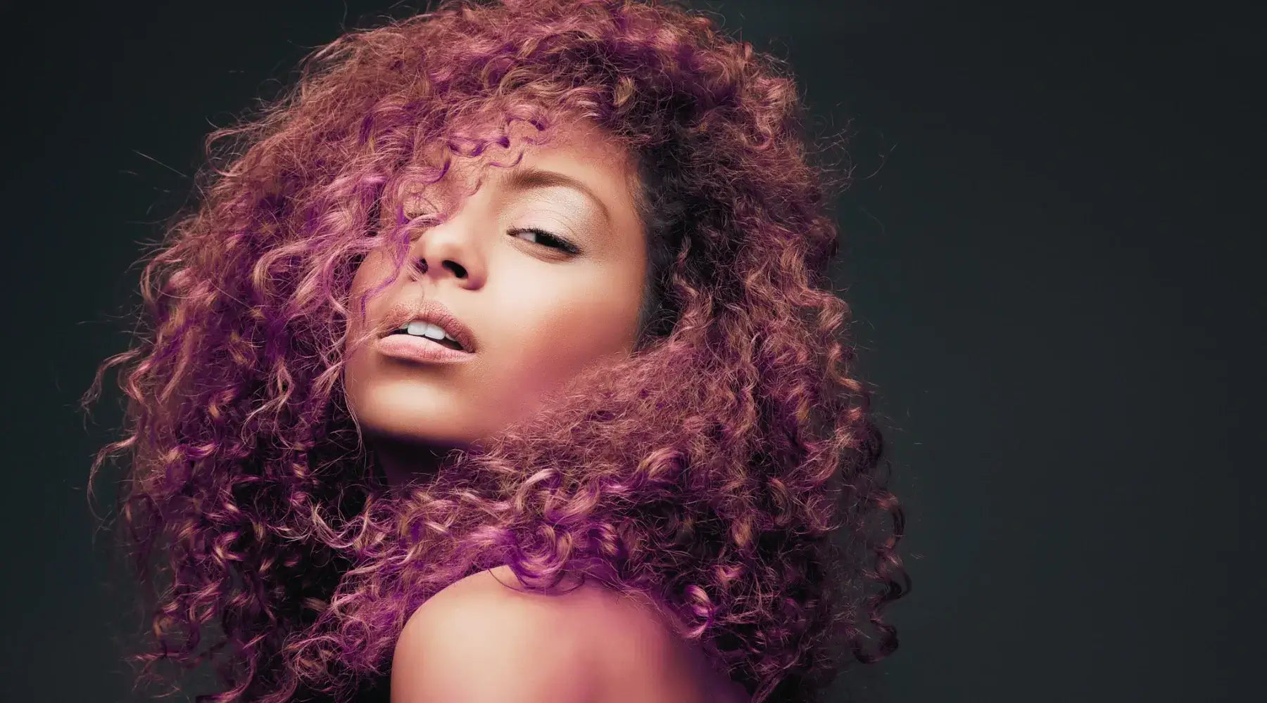 A beautiful Black woman with long deep wave hair looks over her shoulder