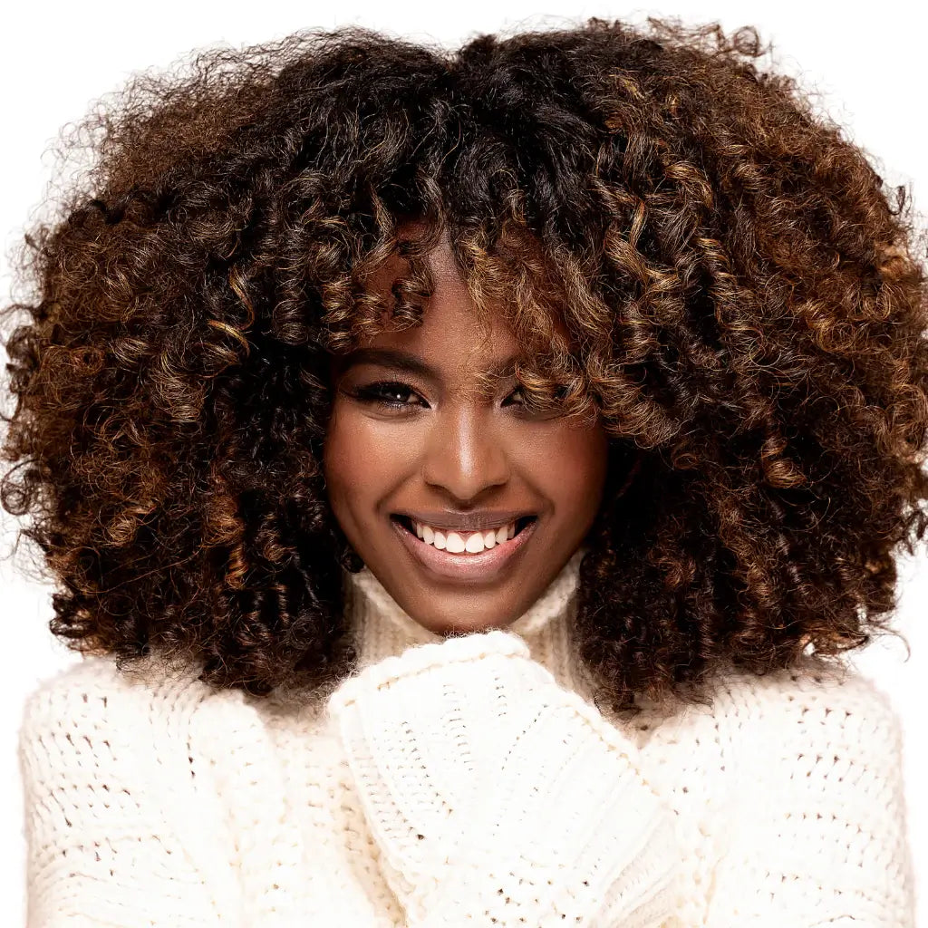 A smiling Black woman with a curly bob hairstyle is a pretty white sweater